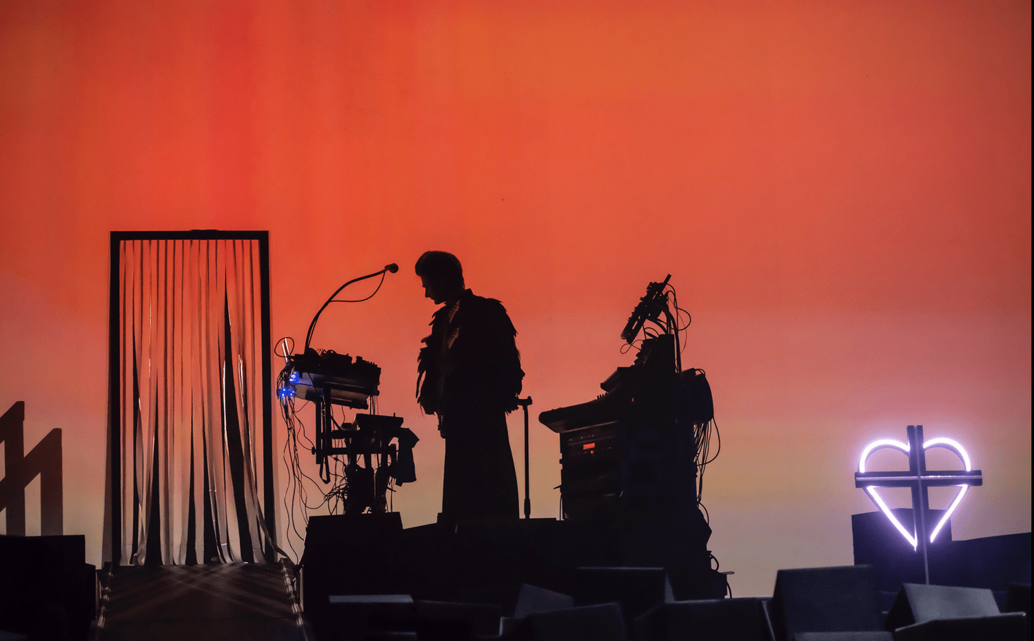 Magnus performing among instruments on a stage illuminated in orange
